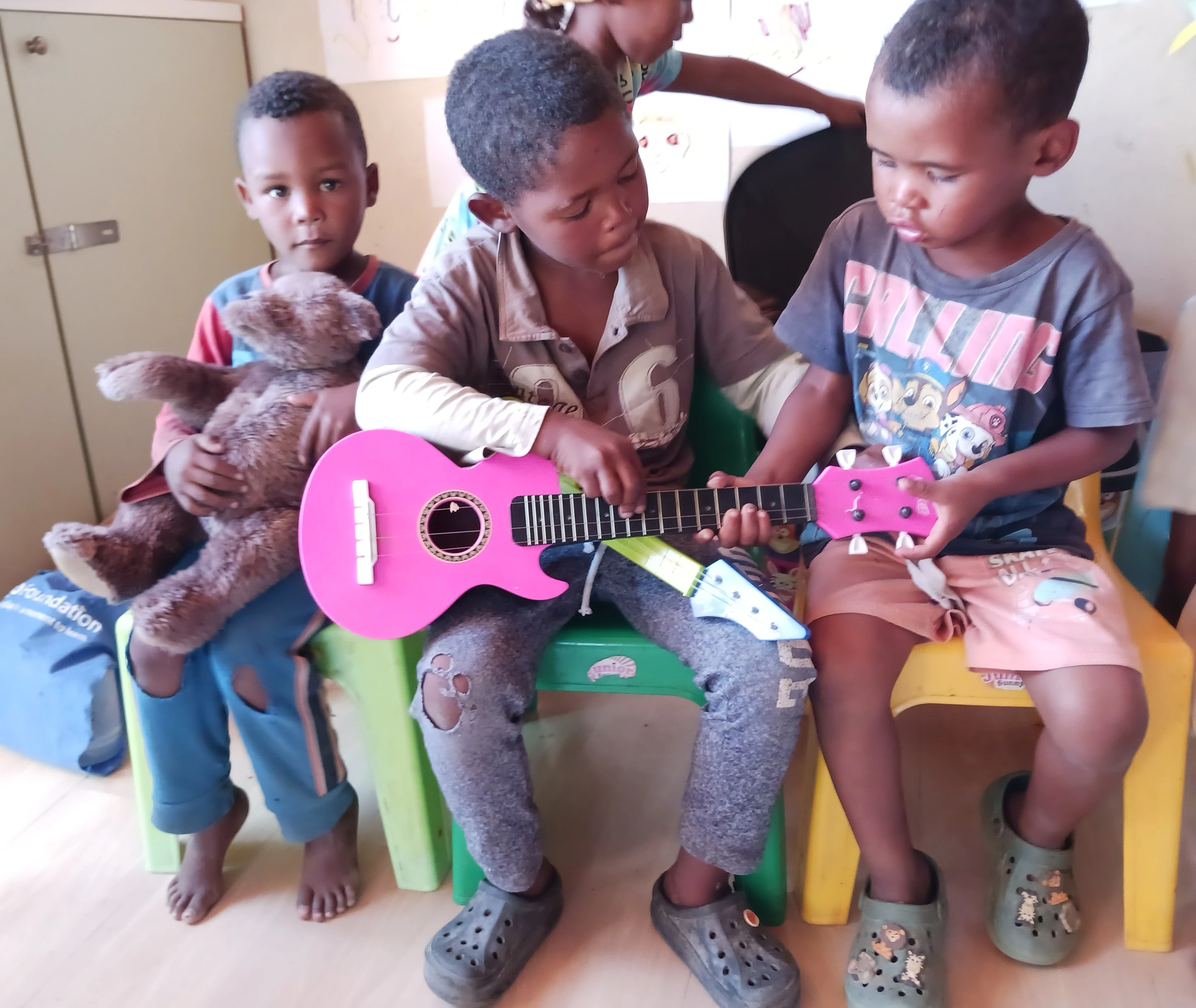 Children playing with a toy guitar and a teddy bear